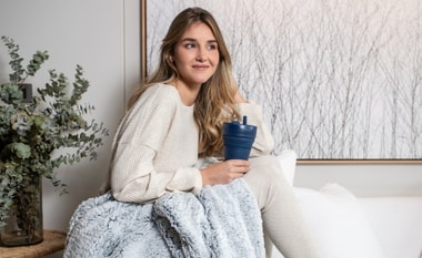 Mujer abrigada con una manta con un vaso en la mano